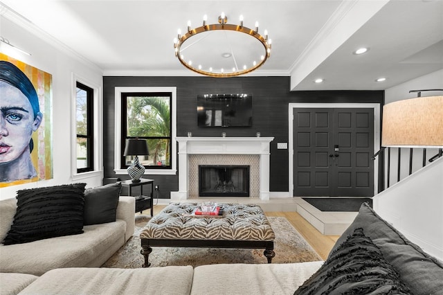 living room with hardwood / wood-style flooring, crown molding, a tiled fireplace, and an inviting chandelier