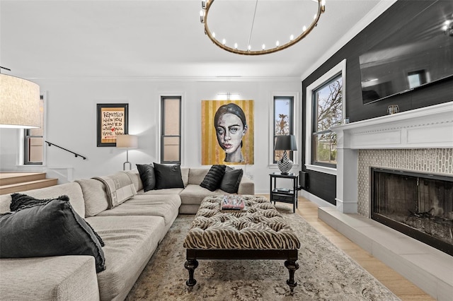 living room featuring light wood-type flooring, a chandelier, crown molding, and a tiled fireplace