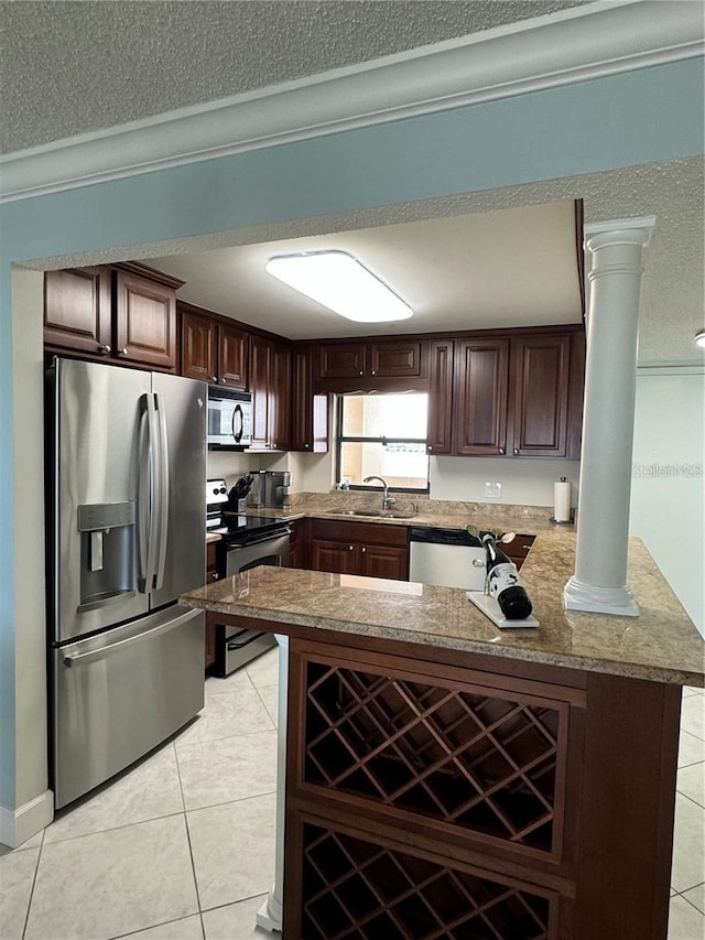 kitchen with light tile patterned floors, kitchen peninsula, decorative columns, stainless steel appliances, and dark brown cabinets