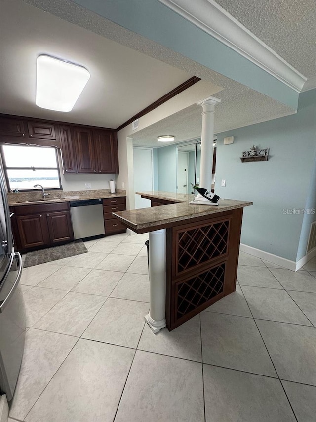 kitchen with a kitchen bar, light tile patterned flooring, crown molding, appliances with stainless steel finishes, and decorative columns