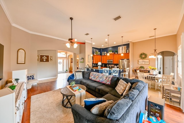 living room with crown molding, ceiling fan with notable chandelier, light hardwood / wood-style flooring, and a towering ceiling