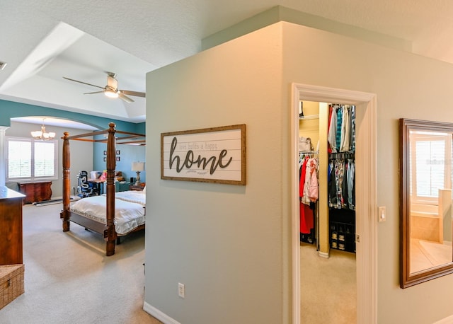 carpeted bedroom with a closet, ceiling fan with notable chandelier, and a raised ceiling