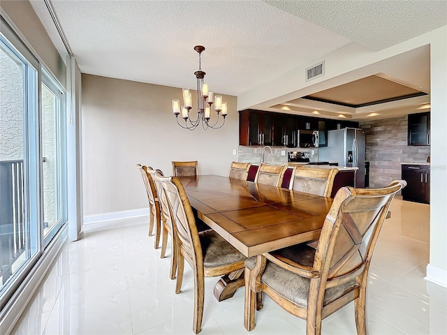 tiled dining space featuring a raised ceiling, sink, a textured ceiling, and a notable chandelier