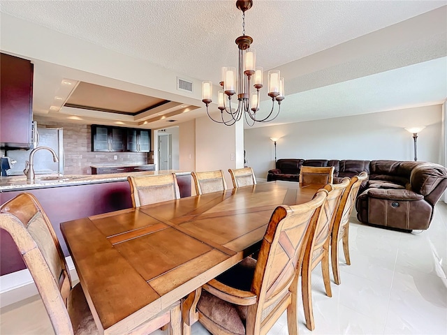 dining room with a textured ceiling, an inviting chandelier, sink, and a tray ceiling