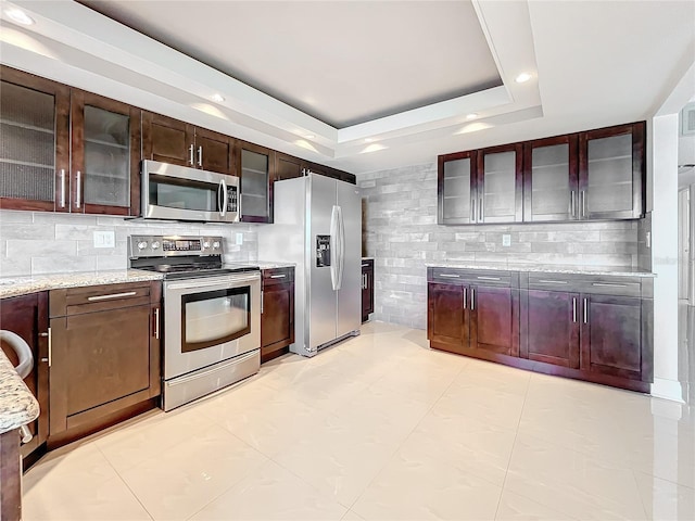 kitchen with light stone countertops, backsplash, stainless steel appliances, a raised ceiling, and light tile patterned floors