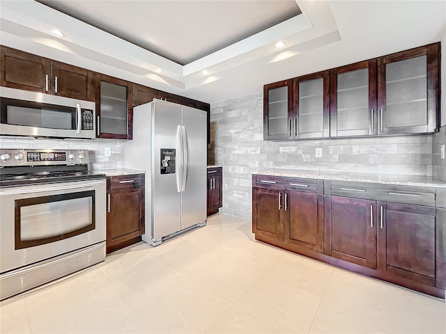 kitchen with light stone countertops, decorative backsplash, stainless steel appliances, and a raised ceiling