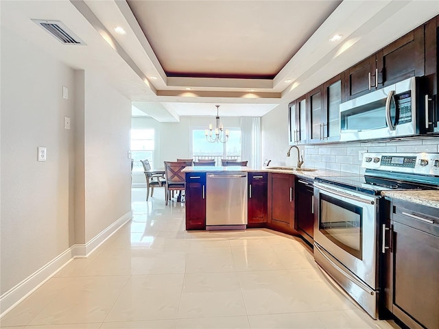 kitchen with sink, an inviting chandelier, decorative light fixtures, a tray ceiling, and appliances with stainless steel finishes