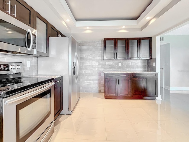 kitchen featuring a raised ceiling, light stone countertops, tasteful backsplash, light tile patterned flooring, and stainless steel appliances