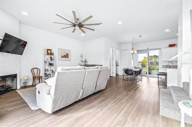 living room with light wood-type flooring, ceiling fan with notable chandelier, and sink