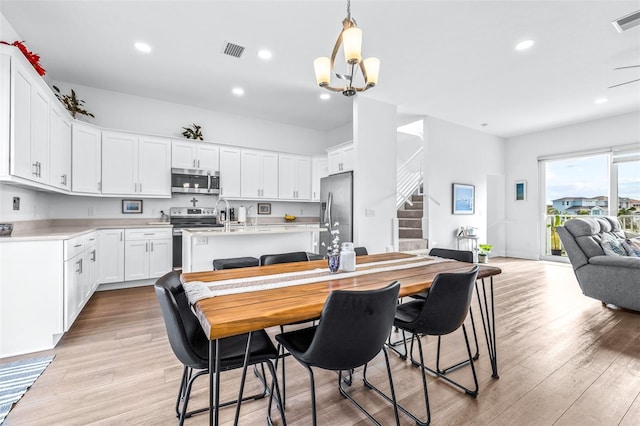 kitchen featuring decorative light fixtures, white cabinetry, appliances with stainless steel finishes, and light hardwood / wood-style flooring