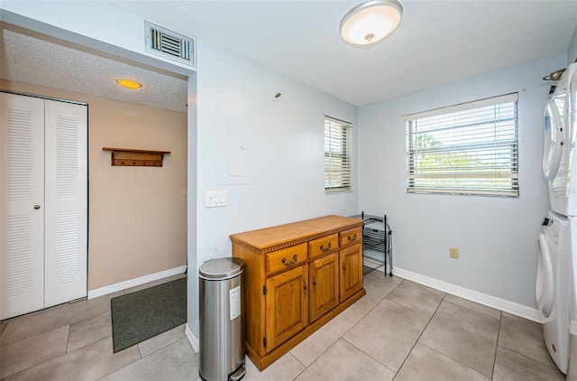 interior space with electric panel, light tile patterned floors, and stacked washing maching and dryer