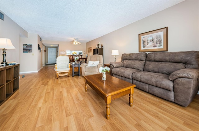 living room with light wood finished floors, ceiling fan, a textured ceiling, and baseboards