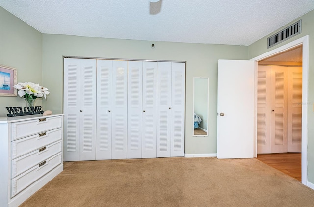 unfurnished bedroom featuring visible vents, light colored carpet, a closet, and a textured ceiling