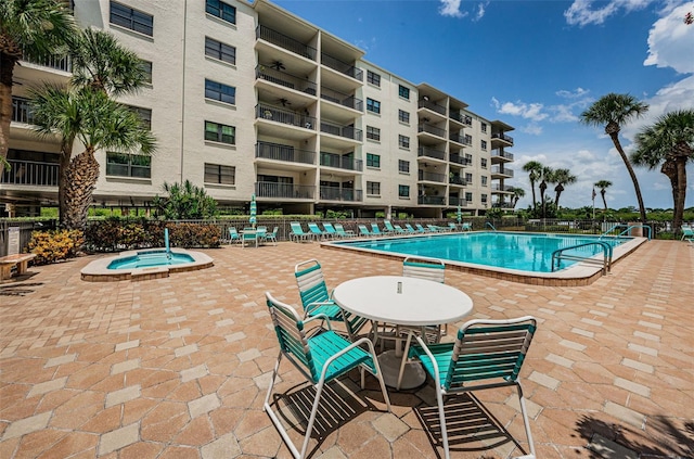 community pool with a patio area, a hot tub, and fence