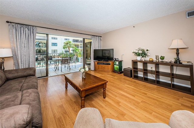 living area featuring visible vents, light wood-type flooring, and a textured ceiling