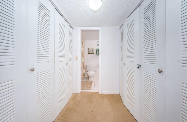 hall with light carpet, a textured ceiling, and baseboards