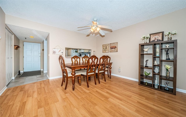 dining space featuring a textured ceiling, a ceiling fan, baseboards, and wood finished floors