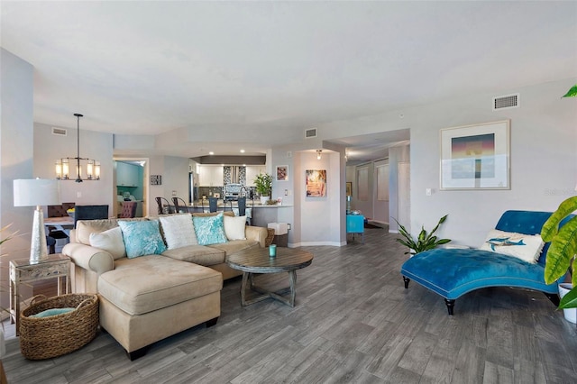 living area with visible vents, baseboards, a notable chandelier, and wood finished floors