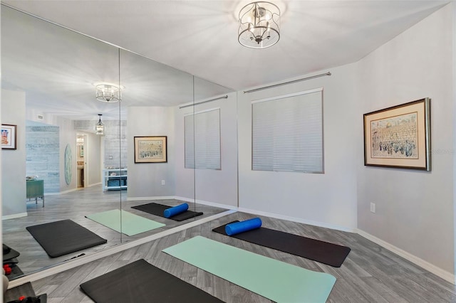 exercise area featuring a notable chandelier, wood finished floors, and baseboards