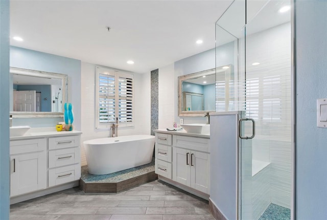 full bathroom featuring wood finish floors, a freestanding tub, two vanities, a stall shower, and a sink