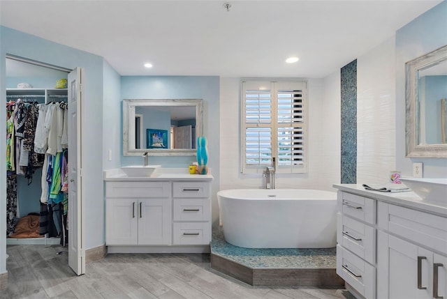 bathroom featuring wood finished floors, a freestanding tub, two vanities, a sink, and a walk in closet