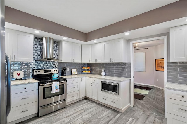 kitchen with backsplash, light wood-style floors, white cabinets, stainless steel appliances, and wall chimney exhaust hood