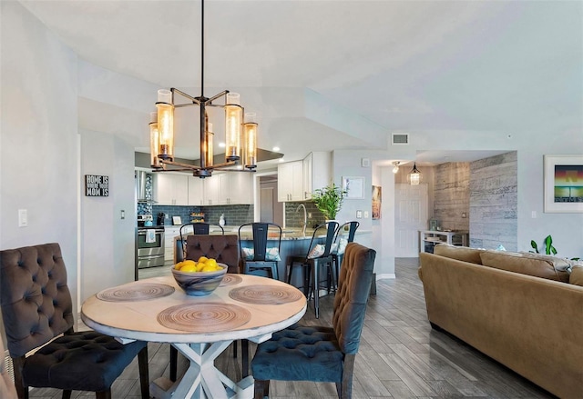 dining space featuring visible vents, a notable chandelier, wood finished floors, and vaulted ceiling