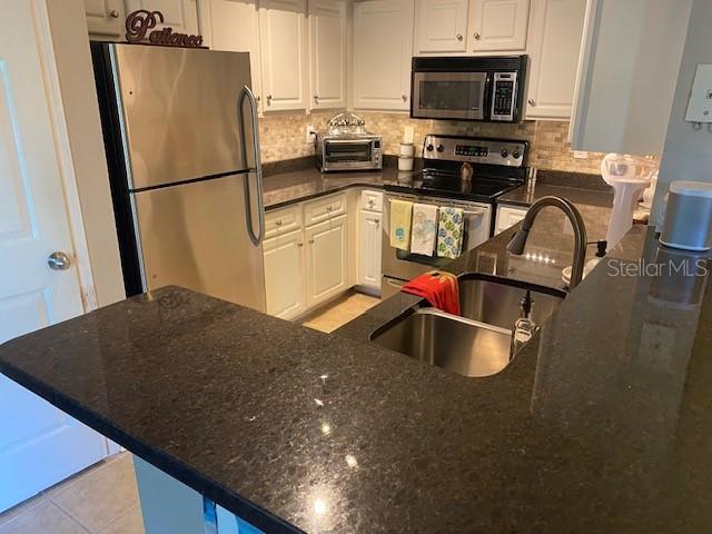 kitchen with sink, stainless steel appliances, tasteful backsplash, dark stone countertops, and white cabinets