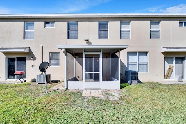 rear view of property with central AC, a sunroom, and a lawn