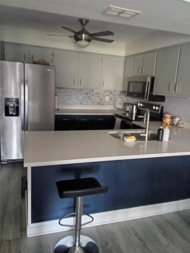 kitchen featuring wood-type flooring, ceiling fan, sink, backsplash, and stainless steel appliances