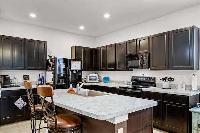 kitchen featuring a kitchen island with sink, sink, black appliances, and a kitchen bar