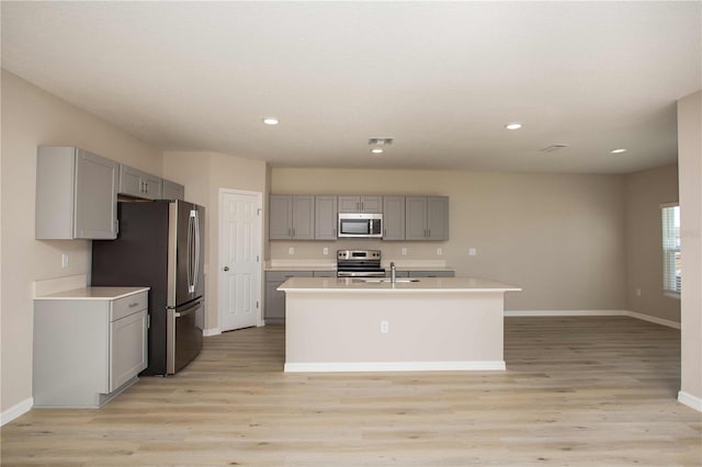 kitchen with gray cabinets, a kitchen island with sink, light hardwood / wood-style flooring, and stainless steel appliances