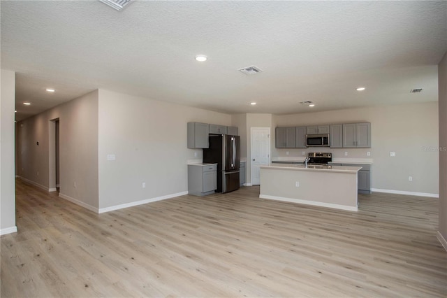 kitchen featuring appliances with stainless steel finishes, gray cabinets, light hardwood / wood-style flooring, and a kitchen island with sink