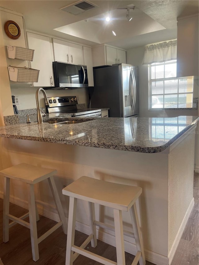 kitchen featuring a kitchen breakfast bar, kitchen peninsula, white cabinets, and stainless steel appliances