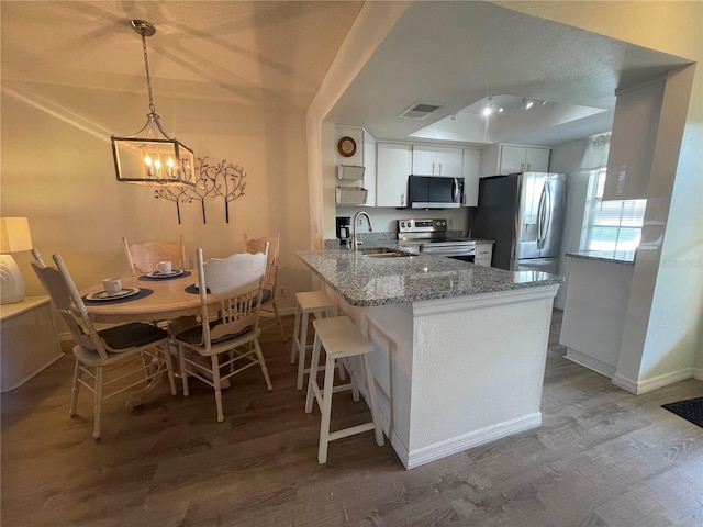 kitchen featuring light stone countertops, stainless steel appliances, sink, white cabinetry, and hanging light fixtures