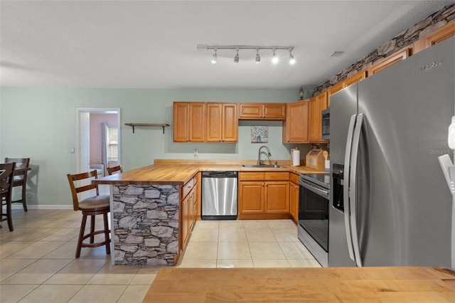 kitchen with light tile patterned flooring, appliances with stainless steel finishes, sink, and wood counters