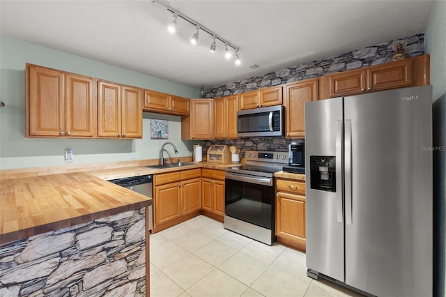 kitchen featuring light tile patterned flooring, wood counters, sink, stainless steel appliances, and backsplash