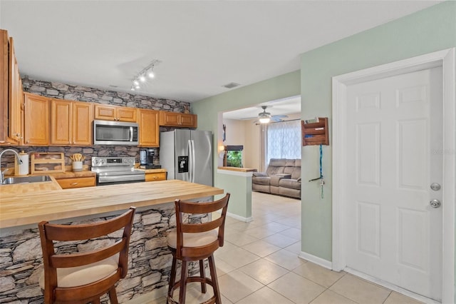 kitchen with wood counters, sink, light tile patterned floors, stainless steel appliances, and decorative backsplash