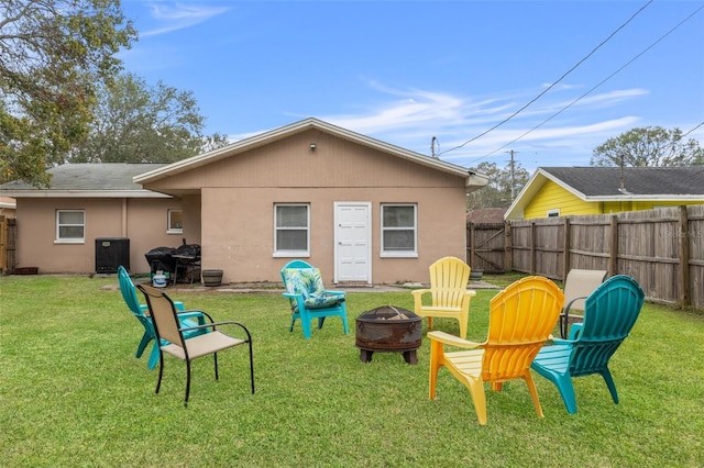 back of property with central AC unit, a fire pit, and a lawn