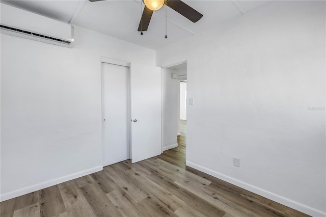 unfurnished bedroom featuring ceiling fan, a wall mounted AC, light hardwood / wood-style flooring, and a closet