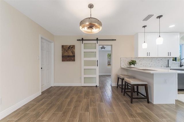 kitchen featuring kitchen peninsula, a kitchen bar, a barn door, decorative light fixtures, and white cabinetry