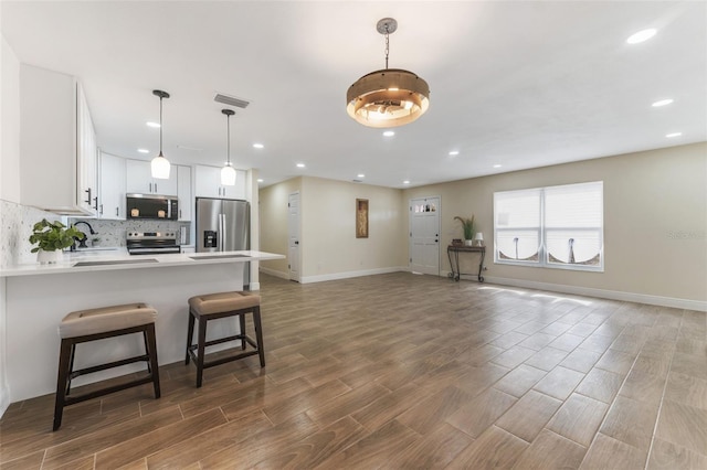 kitchen featuring white cabinetry, hanging light fixtures, kitchen peninsula, a kitchen bar, and appliances with stainless steel finishes