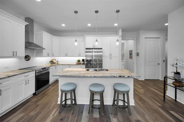 kitchen featuring pendant lighting, appliances with stainless steel finishes, wall chimney exhaust hood, white cabinetry, and a kitchen island with sink