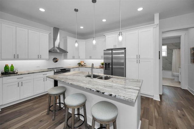 kitchen with decorative light fixtures, wall chimney range hood, sink, appliances with stainless steel finishes, and white cabinets