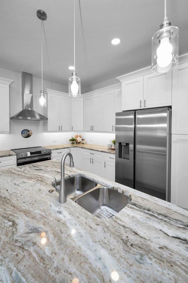 kitchen with hanging light fixtures, white cabinets, appliances with stainless steel finishes, and wall chimney exhaust hood