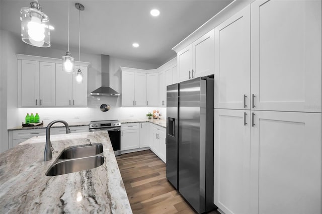 kitchen with wall chimney range hood, sink, white cabinetry, hanging light fixtures, and stainless steel appliances