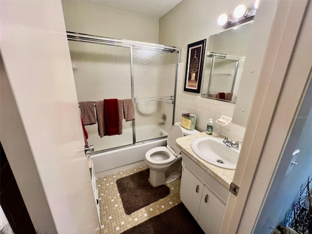 full bathroom featuring toilet, vanity, tile walls, tile patterned flooring, and combined bath / shower with glass door