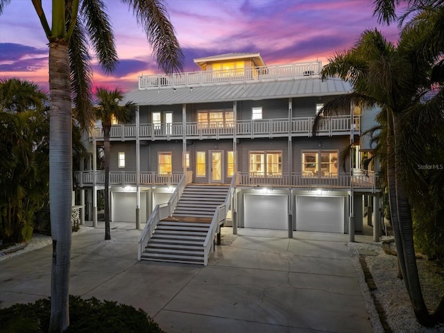 front of house at dusk featuring stairway, driveway, a balcony, and an attached garage