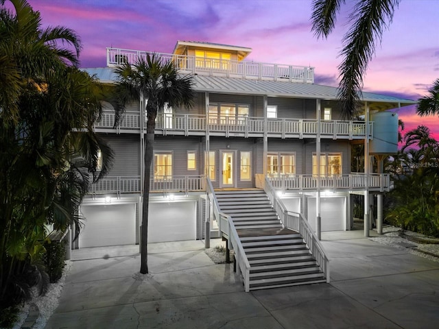 back house at dusk featuring a garage, a balcony, and covered porch