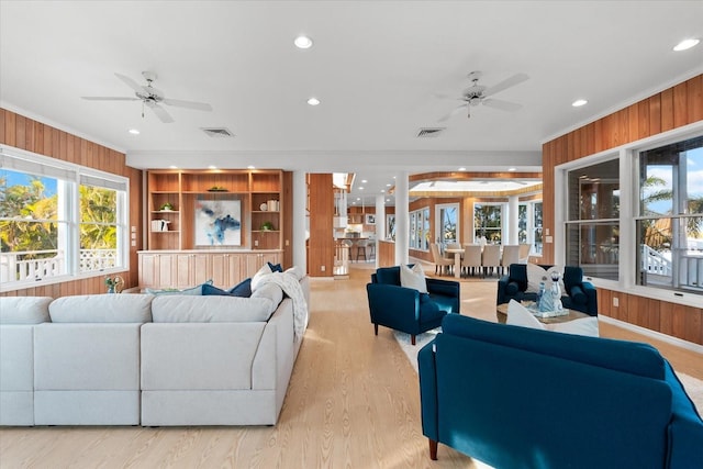 living room with light hardwood / wood-style flooring, wooden walls, ornamental molding, and ceiling fan